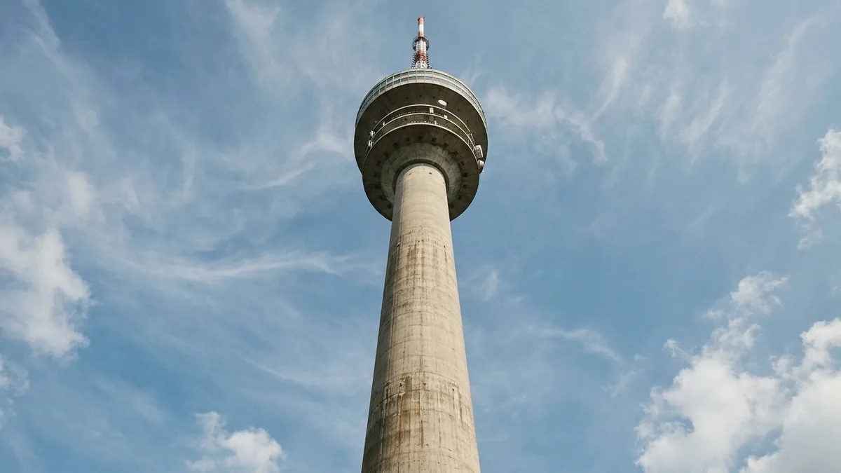 Blick von unten am Betonschaft eines Fernsehturms hinauf zu Kanzel und Antenne vor blauem Himmel