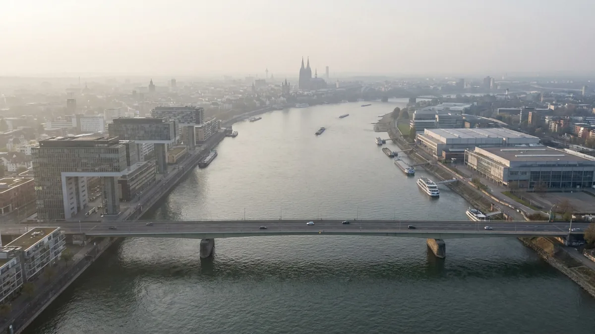Luftaufnahme des Rheins mit einer Brücke, links die Kranhäuser, in der Ferne Dom und Fernsehturm im Dunst