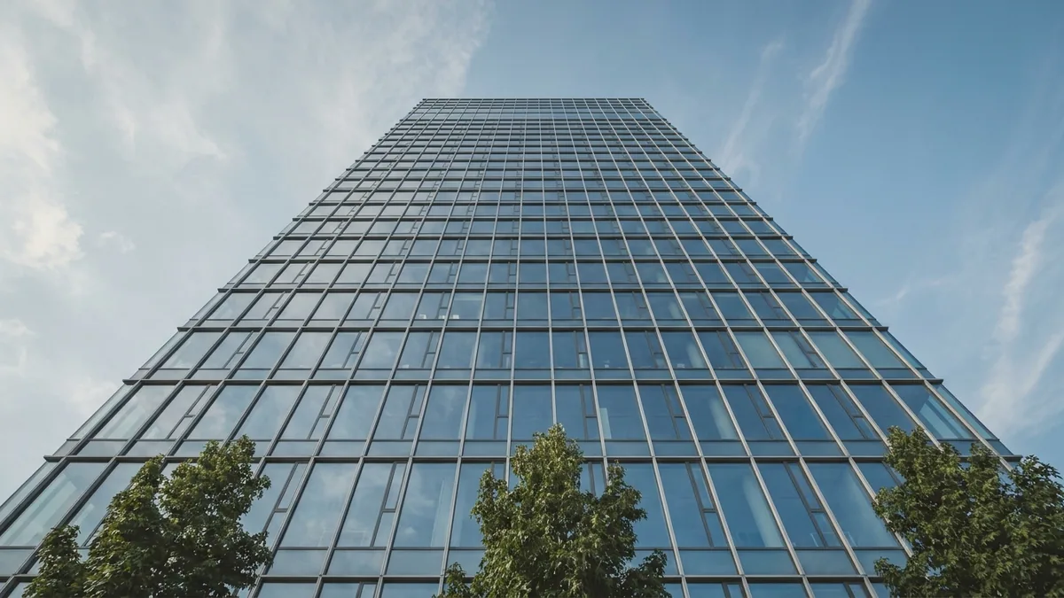 Glasfassade eines Bürohochhauses aus der Froschperspektive vor blauem Himmel, unten Baumkronen