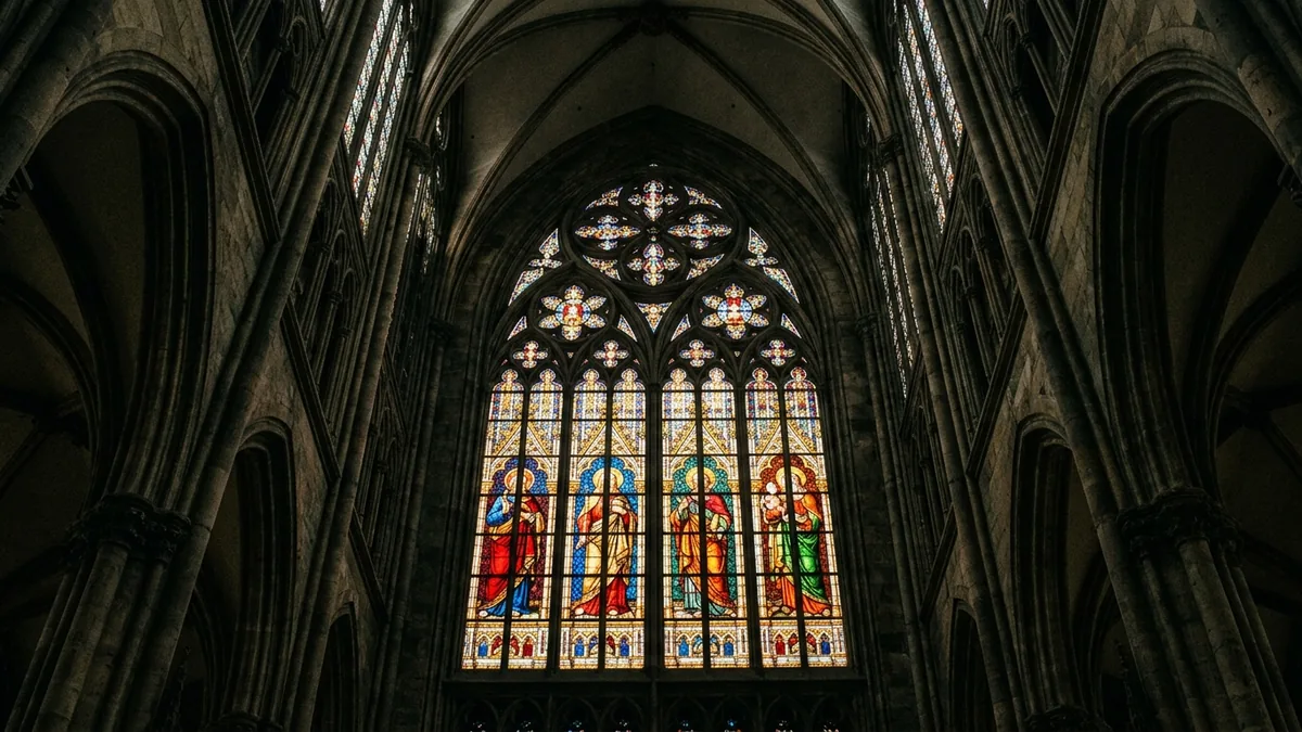 Hohes Buntglasfenster mit vier stehenden Figuren, von unten im Gegenlicht fotografiert.
