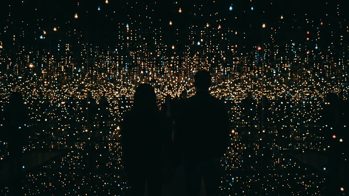 Silhouetten von Besuchern in einem verspiegelten Raum voller kleiner Lichtpunkte