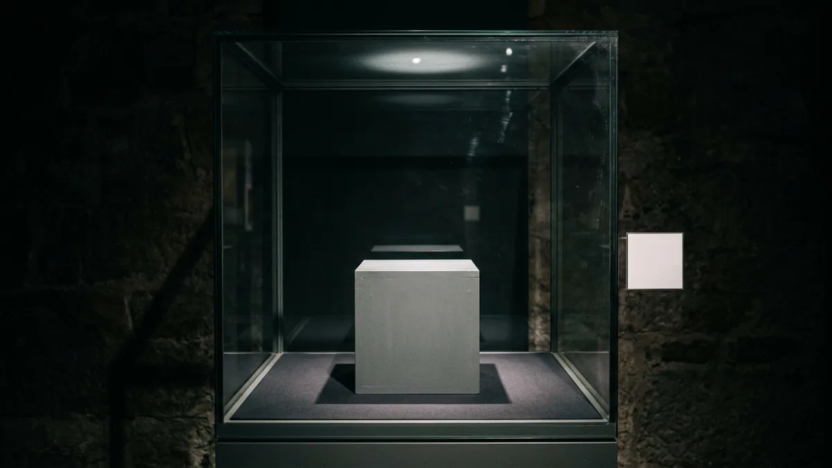 Leere Vitrine mit Sockel und unbeschriftetem Schild in einem abgedunkelten Ausstellungsraum
