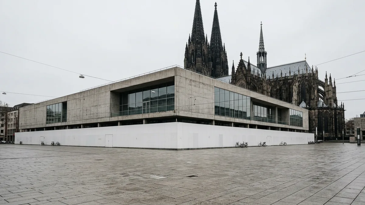 Flacher Museumsbau hinter hohem Bauzaun, dahinter die Türme einer gotischen Kathedrale