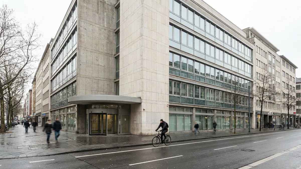 Mehrgeschossiges Bürogebäude mit Natursteinfassade an einer Straßenecke, ein Radfahrer passiert den Eingang