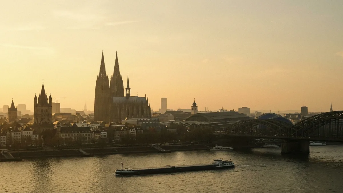 Kölner Altstadtpanorama im Abendlicht mit Dom, Groß St. Martin und Hohenzollernbrücke, auf dem Rhein Frachtschiffe