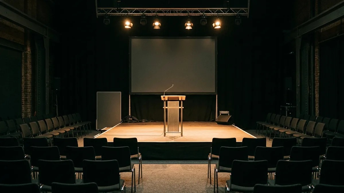 Leere Bühne mit Leinwand und Stuhlreihen vor einer Veranstaltung